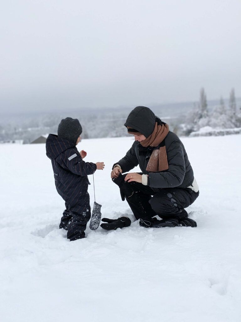 Vrouw en kind doen handschoenen aan in sneeuw
